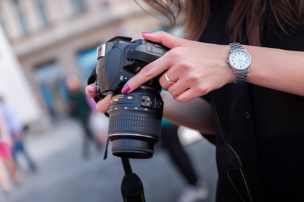 gallery-02 A woman adjusting a DSLR camera outdoors, focusing on her hands and device. Perfect for photography themes.