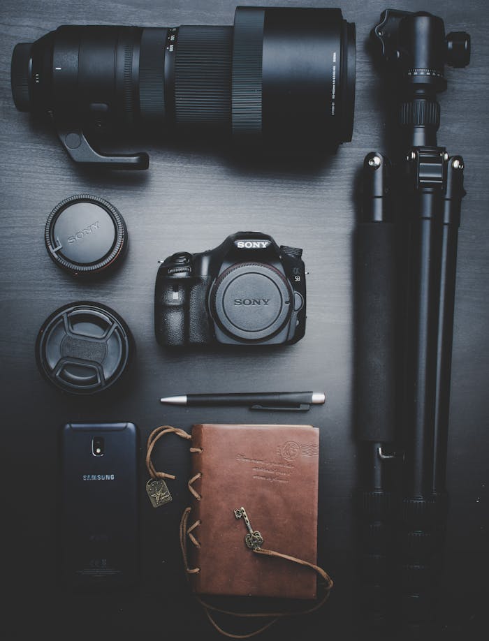 gallery-04 Flat lay of photography equipment including a DSLR, lenses, and accessories on a table.